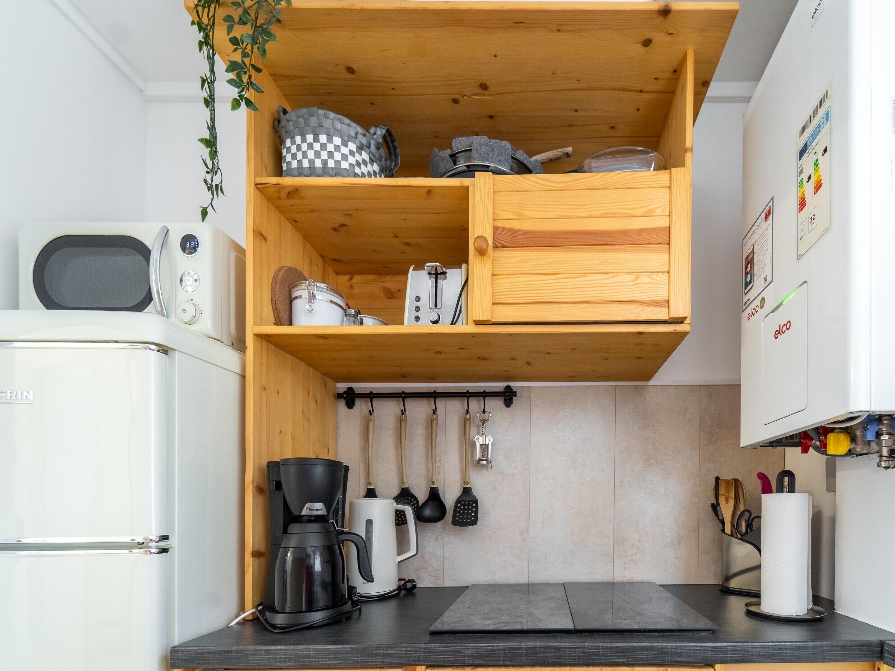 A compact kitchen with a microwave, coffee maker, and hanging utensils.