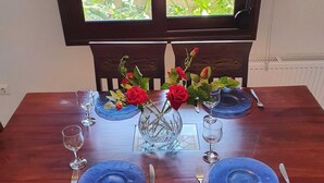 A dining table set with blue plates, silverware, and wine glasses, adorned with red roses in a clear vase. - Apartment in Loutra Elenis With Garden (Corinth)