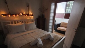 A neatly made bed with a white headboard, a brown throw blanket, and two rolled towels. There is a string of lights on the ceiling above the bed. - Apartment in Loutra Elenis With Garden (Corinth)