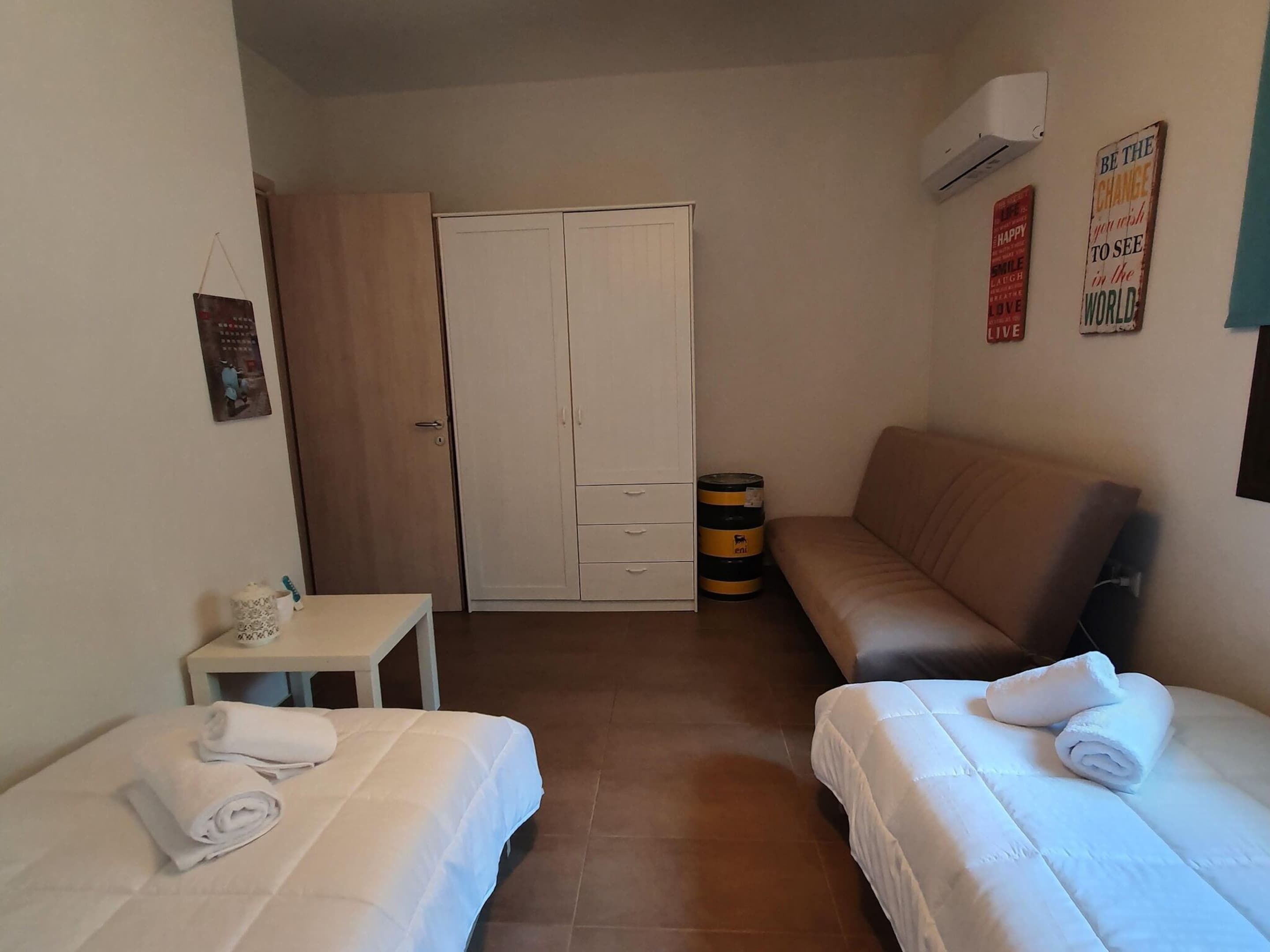 Ein kleines, sauberes Zimmer mit zwei Betten, einer Schlafcouch, einem kleinen Tisch und einem Kleiderschrank.