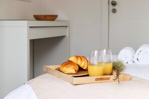 Una bandeja de madera con cruasanes y un vaso de zumo de naranja sobre una cama.