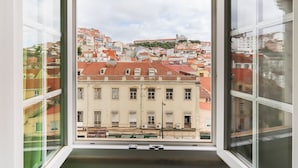A view from a window overlooking a cityscape with red-roofed buildings and a hill with a church. - Downtown Palma Suites by Homing (Lisbon)