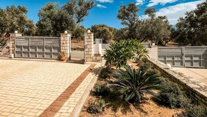 A gated entrance with a paved driveway leading to a building, surrounded by trees and a clear sky. - Villa in Crete With Stunning Rural Views (Rethymno)