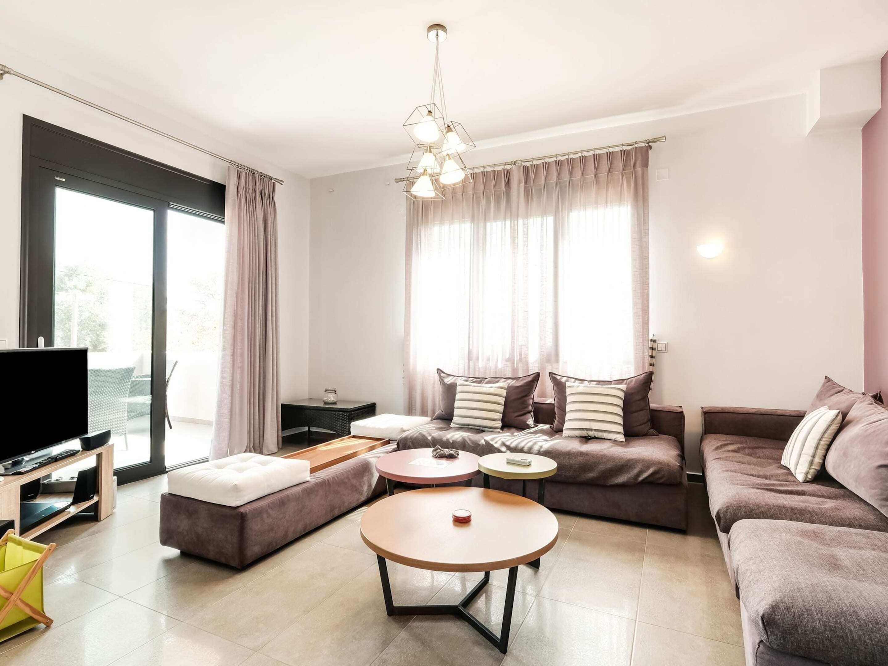 A modern living room with a sofa, two round tables, a TV, and a balcony with curtains.