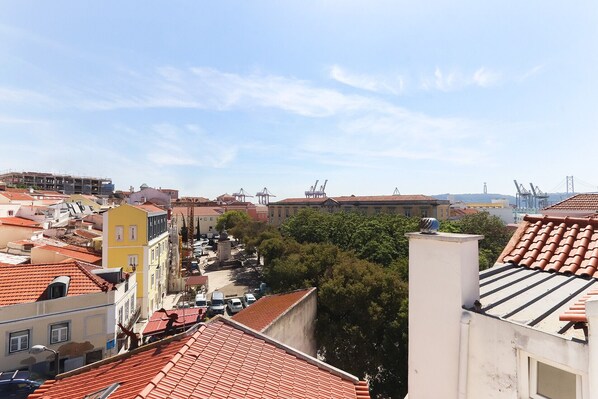 Paisagem urbana com telhados vermelhos, mistura de edifícios antigos e modernos, e guindastes ao longe.
