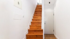 Una escalera de madera en un pasillo con paredes blancas y una puerta al final.