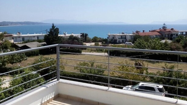 A balcony with a metal railing overlooking a residential area with houses and a view of the sea. - Cheerful Holiday Home in Preveza With Garden (Preveza)