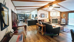 Amplia sala de estar con techo de madera, chimenea y comedor con mesa y sillas.