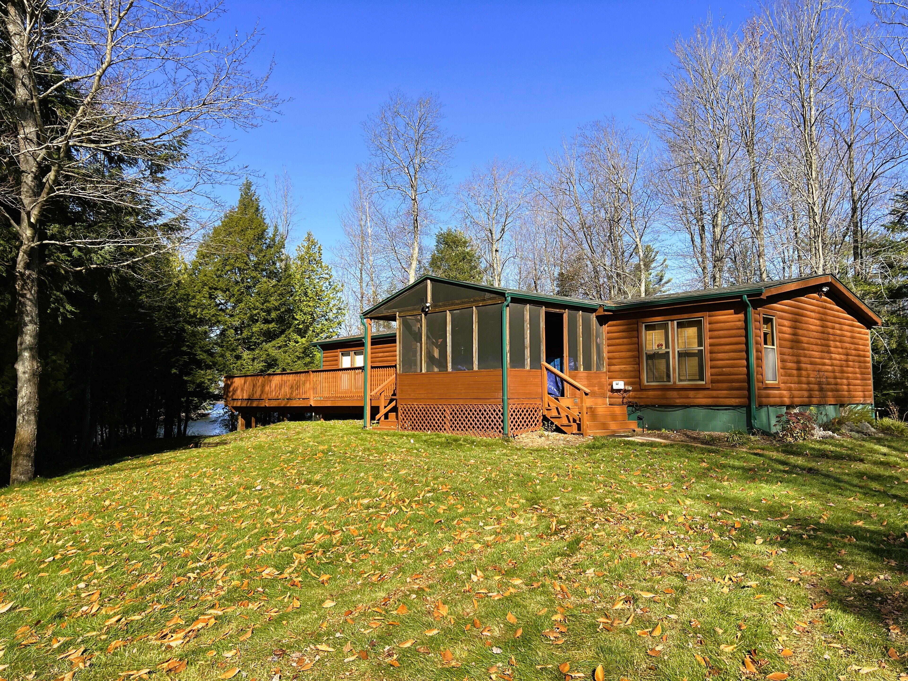 Une cabane en bois dotée d’une terrasse, entourée d’arbres et d’une zone herbeuse.
