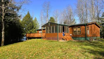 Une cabane en bois dotée d’une terrasse, entourée d’arbres et d’une zone herbeuse.