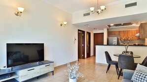 Una sala de estar moderna con un televisor de pantalla plana, un comedor con mesa y sillas, y una cocina al fondo.