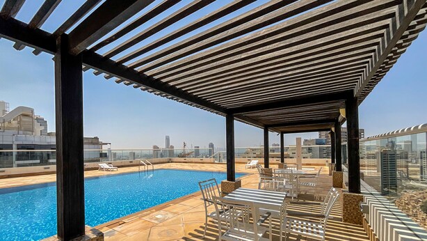 Un área de piscina en la azotea con vista despejada al horizonte de la ciudad, tumbonas y una estructura de pérgola.