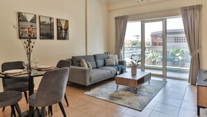Una sala de estar moderna con un sofá gris, una mesa de comedor y sillas. Hay tres cuadros en la pared, un jarrón con ramas y un ventanal con cortinas.
