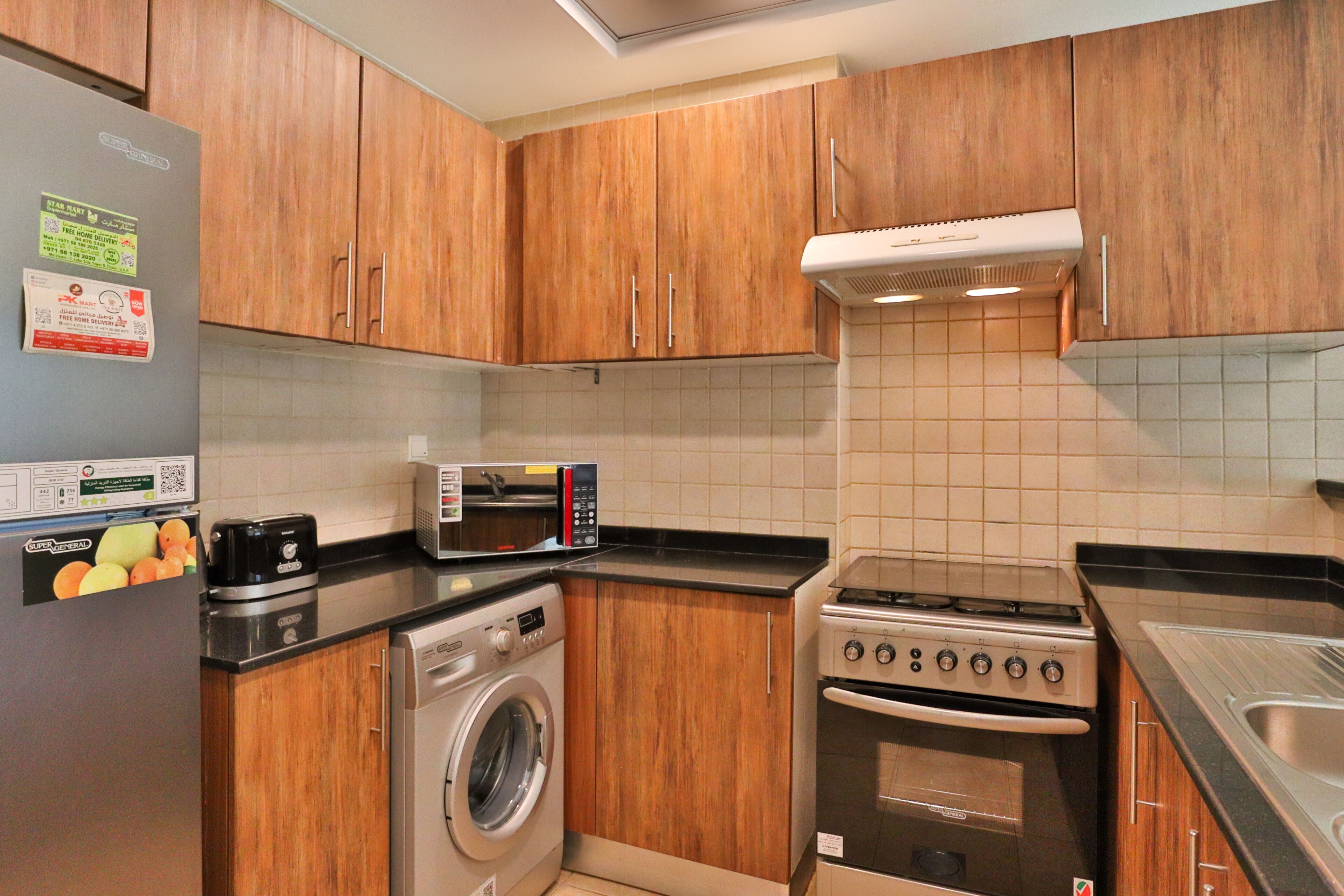 A compact kitchen with wooden cabinets, a built-in washing machine, a microwave, and a stove.