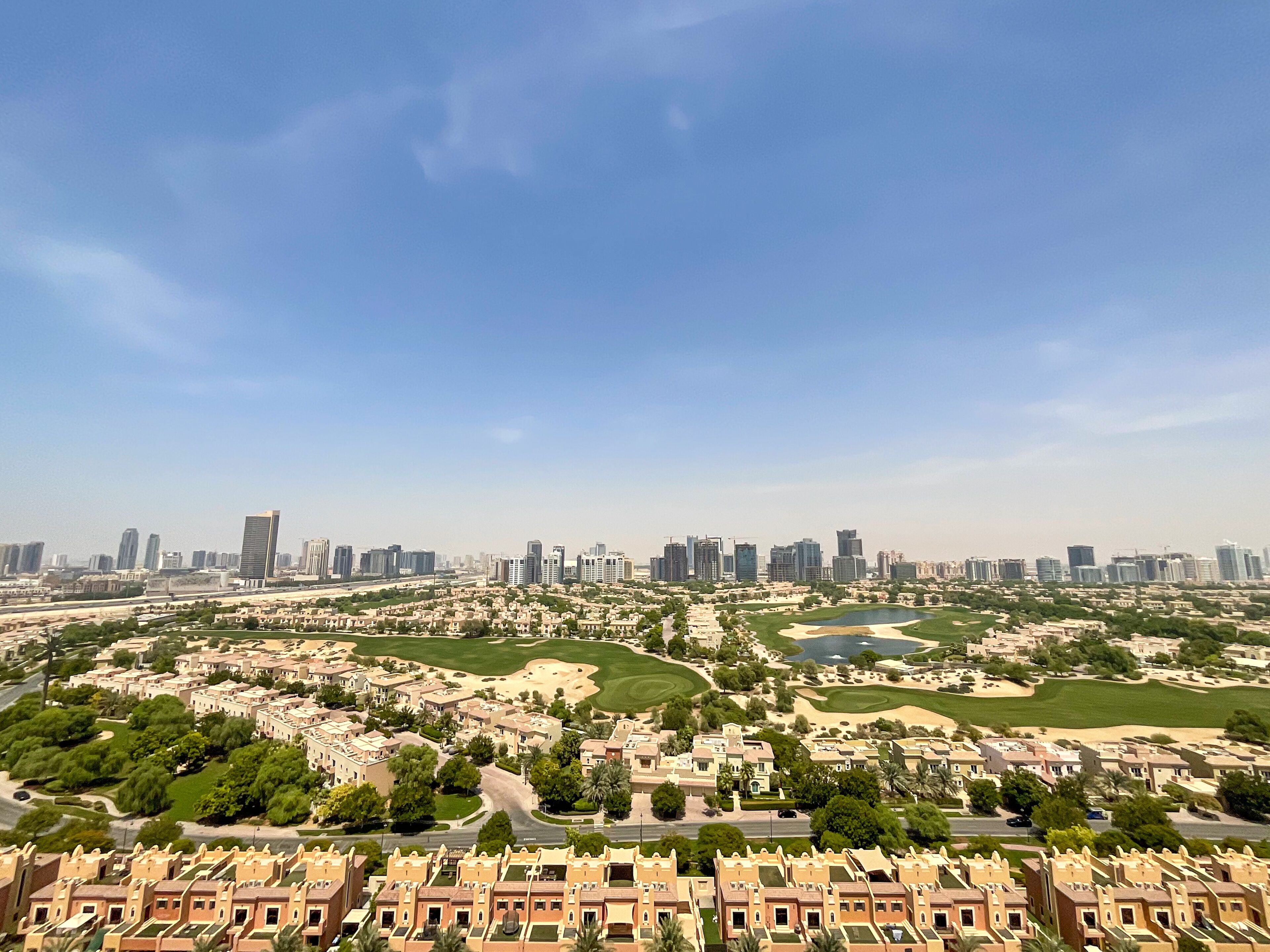 A residential area with modern high-rise buildings, a golf course, and a clear blue sky.