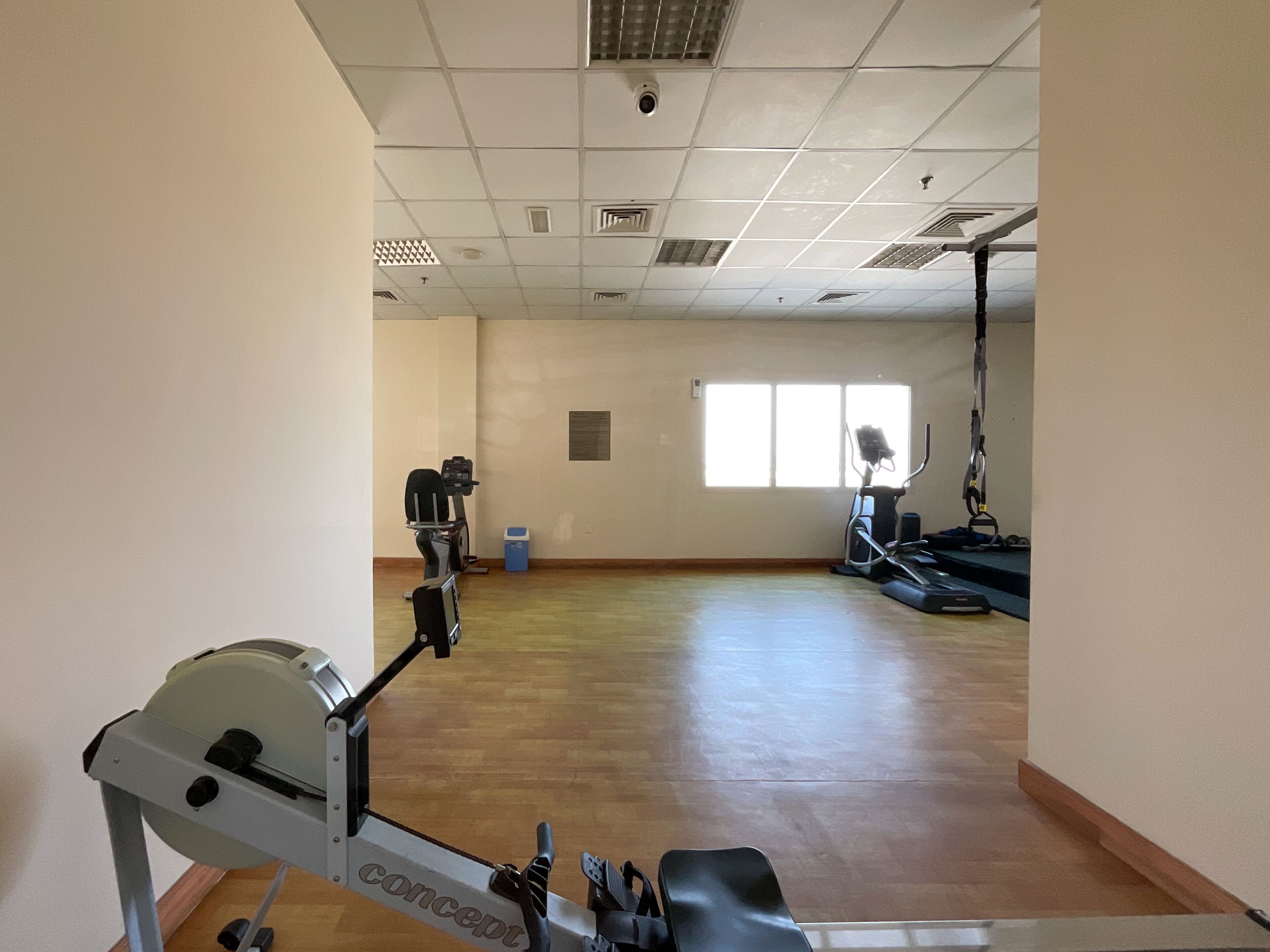 A spacious room with a stationary bike, a treadmill, and a window providing natural light.