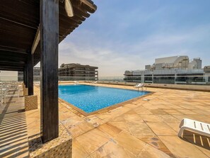 A rooftop pool with clear blue water, surrounded by tiled flooring and white lounge chairs.