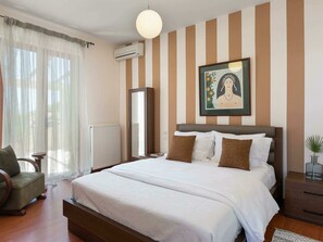 Habitación de hotel con una cama grande, una silla, una mesita de noche, un radiador, una ventana con cortinas translúcidas y un aire acondicionado de pared.