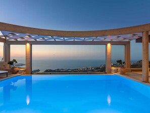 Una piscina infinita con vista al mar y un pueblo costero al atardecer.