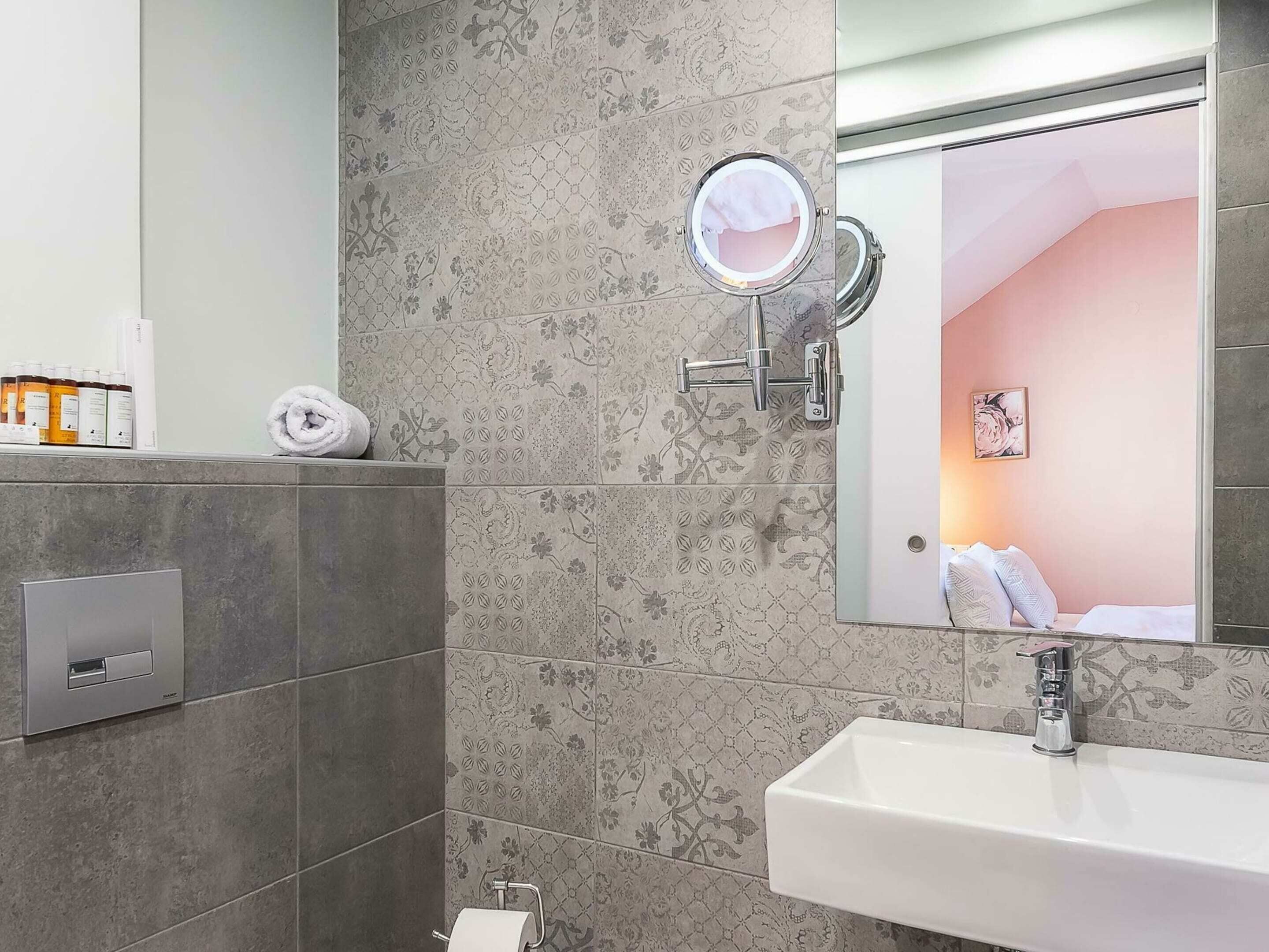 Un baño moderno con pared de azulejos grises, un lavabo blanco, un espejo y un perchero para toallas.