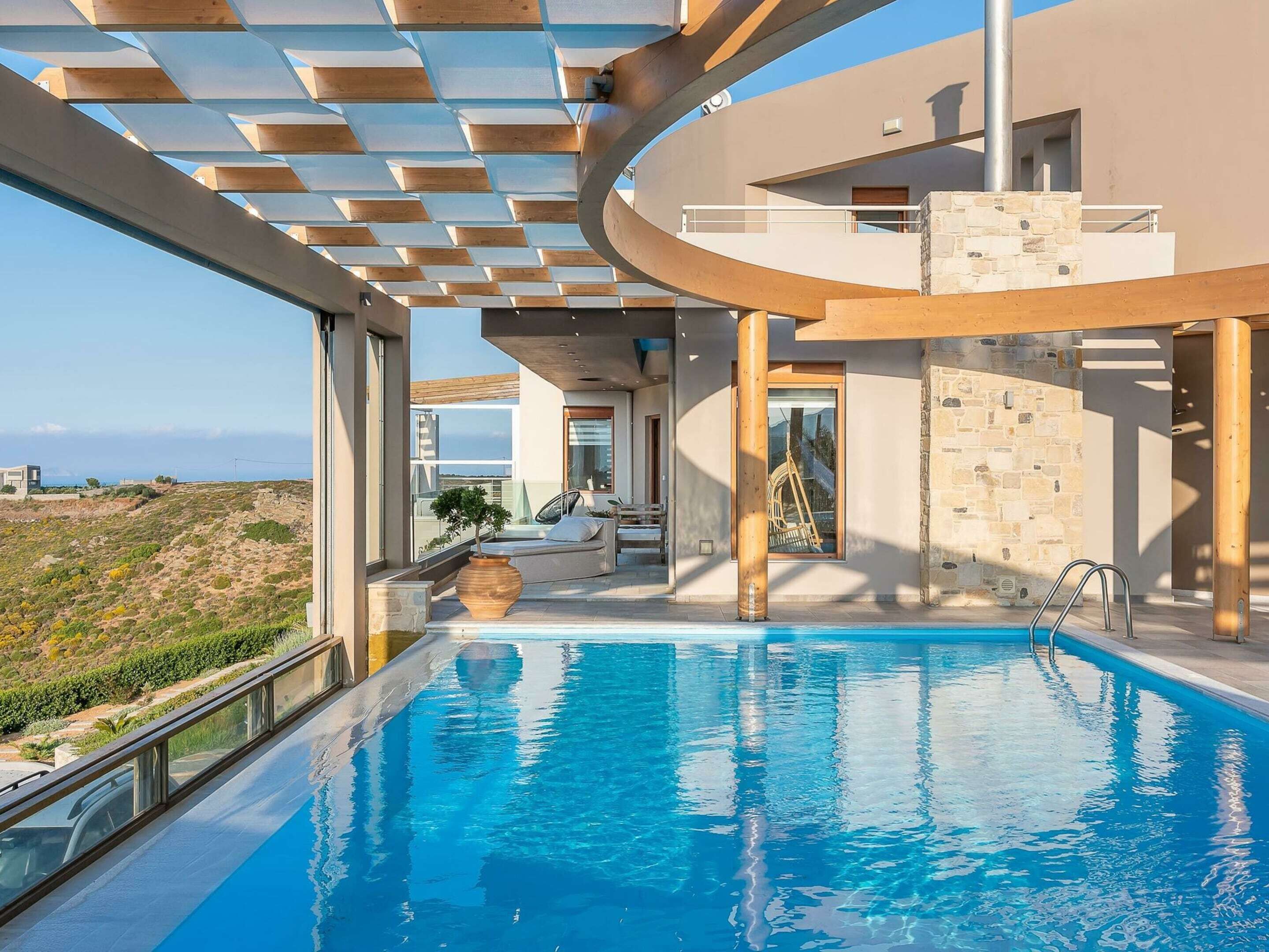 A modern pool area with a clear view of the surrounding landscape, a stone wall, and a wooden deck.