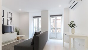 A modern living room with a grey sofa, a flat-screen TV on a white cabinet, a small side table, and a potted plant. - Graça Elegant by Homing (Lisbon)