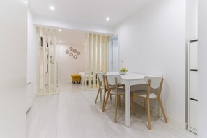 Un'area pranzo moderna con un tavolo e sedie bianche, un pouf giallo e un elemento decorativo a parete.