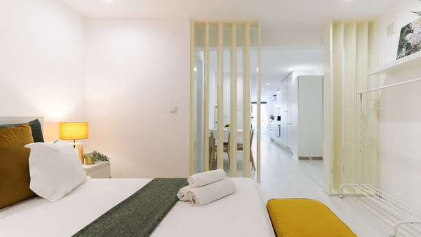 A modern hotel room with a bed, a bedside lamp, a bench, and a view of the hallway and kitchen. - Graça Elegant by Homing (Lisbon)