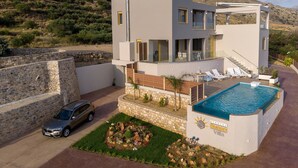 A modern villa with a swimming pool, a stone wall, and a car parked in front.