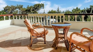 A balcony with wicker furniture and a view of trees and buildings. - Beautiful Holiday Home With Private Pool (Rhodes)
