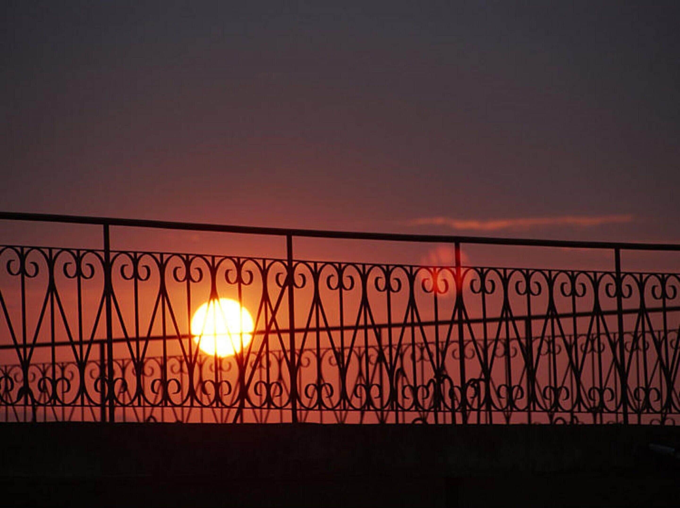 A sunset behind a decorative metal fence.