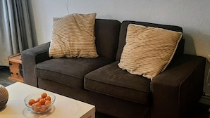 A dark brown sofa with two beige pillows, a white table with a glass bowl of oranges, and a painting on the wall. - Cosy Holiday Home Near the ski Lift (Grossbreitenbach)