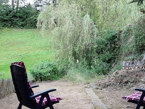 Relax in a serene outdoor space surrounded by lush greenery and a weeping willow tree.