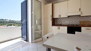 A modern kitchen with a dining area, a sliding glass door leading to a balcony, and a view of a hilly landscape. - 199 Casa a 500m dal Mare a S M di Leuca (Castrignano del Capo)