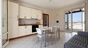 A modern kitchen with white cabinets, a dining area with a white table and chairs, and a large sliding glass door leading to an outdoor balcony. - 199 Casa a 500m dal Mare a S M di Leuca (Castrignano del Capo)