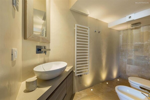 A modern bathroom with a large vessel sink, a mirror, a towel rack, a shower, and a toilet.