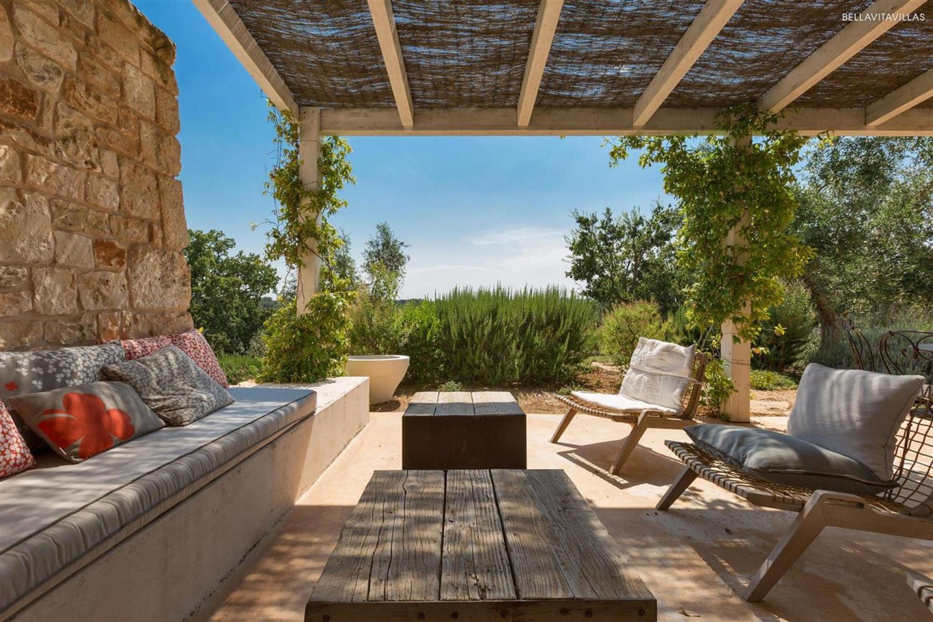 An outdoor patio with a stone wall, a wooden table, and two cushioned chairs.