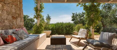 An outdoor patio with a stone wall, a wooden table, and two cushioned chairs.