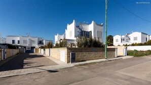 Une rue résidentielle bordée de maisons blanches, avec une chaussée goudronnée et un ciel bleu dégagé.