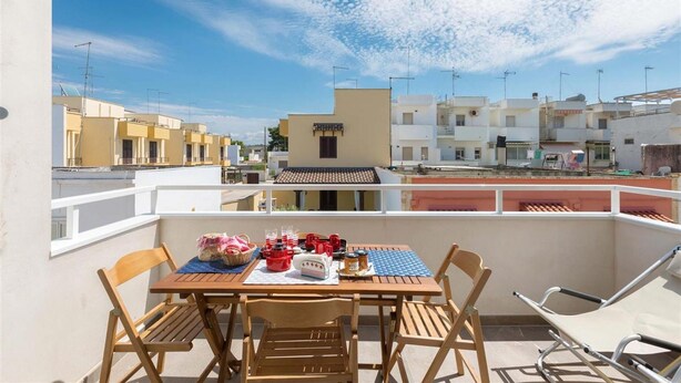 A balcony with a table, chairs, and a view of neighboring buildings. - 1659 Dodger House in Porto Cesareo (Porto Cesareo)