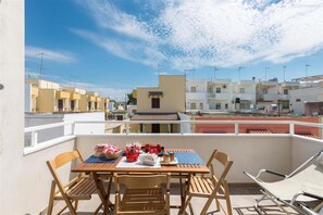 A balcony with a table, chairs, and a view of neighboring buildings. - 1659 Dodger House in Porto Cesareo (Porto Cesareo)