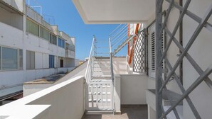 A narrow balcony with a metal railing, a staircase leading to an upper level, and a view of a building with multiple windows. - 1659 Dodger House in Porto Cesareo (Porto Cesareo)