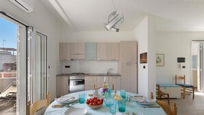A modern kitchen with sliding doors, a dining area with a table set for four, and a small seating area with chairs. - 1659 Dodger House in Porto Cesareo (Porto Cesareo)