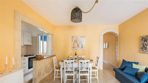 A dining area with a table set for four, white chairs, a chandelier, and a painting on the wall. - 1700 Casa Mya in Lido Marini (Salve)