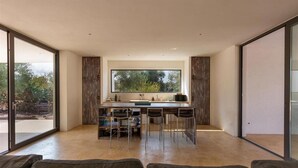 A modern kitchen with a large window, a dining area with bar stools, and a sliding glass door leading to an outdoor area.