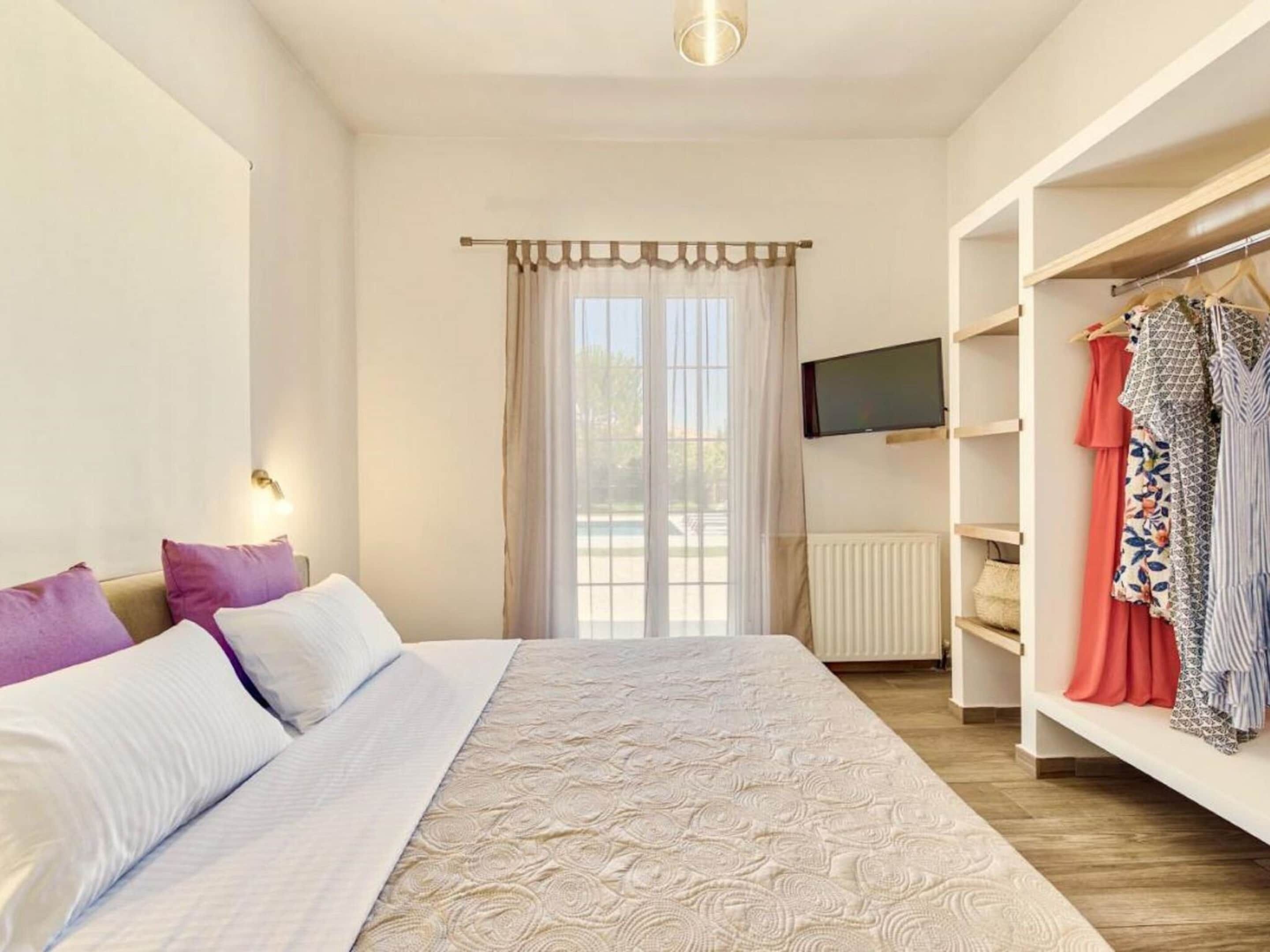A bedroom with a bed, a wardrobe, a television, and a window with curtains.