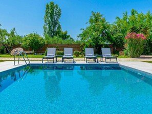 A swimming pool with three lounge chairs and a metal ladder.