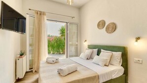 A bedroom with a green upholstered bed, a flat-screen TV mounted on the wall, and a window with a view of greenery outside. - Scenic Villa in Pigadakia With Private Pool (Zakynthos)