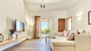 A modern living room with a sofa, a coffee table, and a TV mounted on the wall. - Scenic Villa in Pigadakia With Private Pool (Zakynthos)