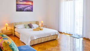 A bedroom with a bed, two bedside lamps, a colorful cushion, a wooden floor, and a window with sheer curtains. - Holiday Home in Senj With Pool Near Beach (Senj)
